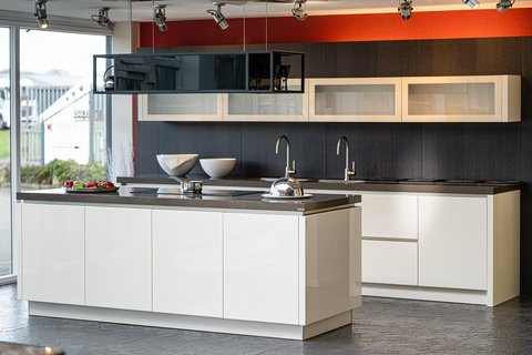 Eine moderne Küche mit weißen Hochglanzfronten, einer dunklen Arbeitsplatte und einer Kücheninsel mit Spüle und Kochfeld