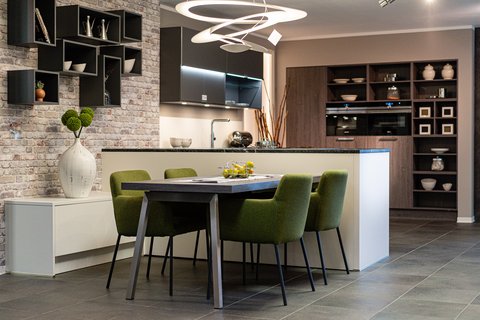Ein moderner Essbereich mit einem grauen Tisch und grünen Stühlen, angrenzend an eine Küche mit schwarzen Arbeitsplatten und dunklen Schränken