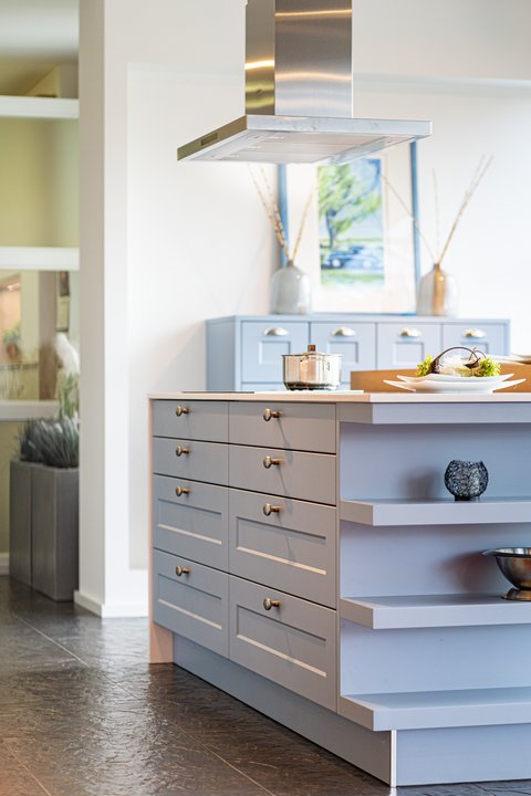 Detailansicht einer modernen Kücheninsel in hellem Blau-Grau mit goldenen Griffen und einer Edelstahl-Dunstabzugshaube