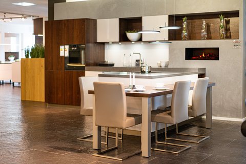 Ein offener, moderner Küchen- und Essbereich mit einer hellen Kücheninsel, einem Esstisch mit vier Stühlen und einem eingebauten Kamin