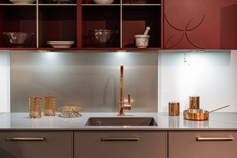 Eine Nahaufnahme eines modernen Küchenspülbereichs mit einem dunklen Spülbecken, einem kupferfarbenen Wasserhahn und dunklen roten Hängeschränken